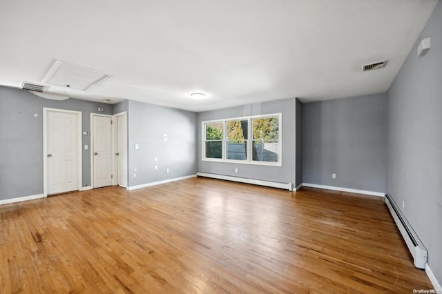 unfurnished room featuring a baseboard heating unit, light wood-style floors, baseboard heating, baseboards, and visible vents