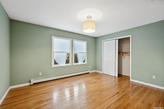 unfurnished bedroom featuring baseboards, wood finished floors, a baseboard heating unit, and a closet