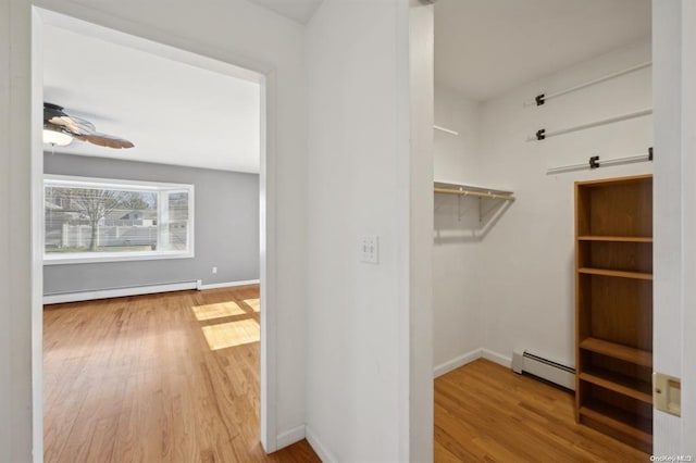 spacious closet with a baseboard radiator, wood finished floors, ceiling fan, and baseboard heating