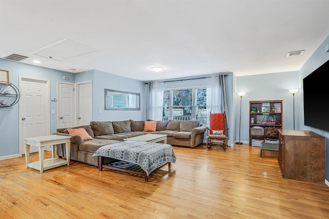 living room featuring attic access, visible vents, baseboards, and light wood-style floors