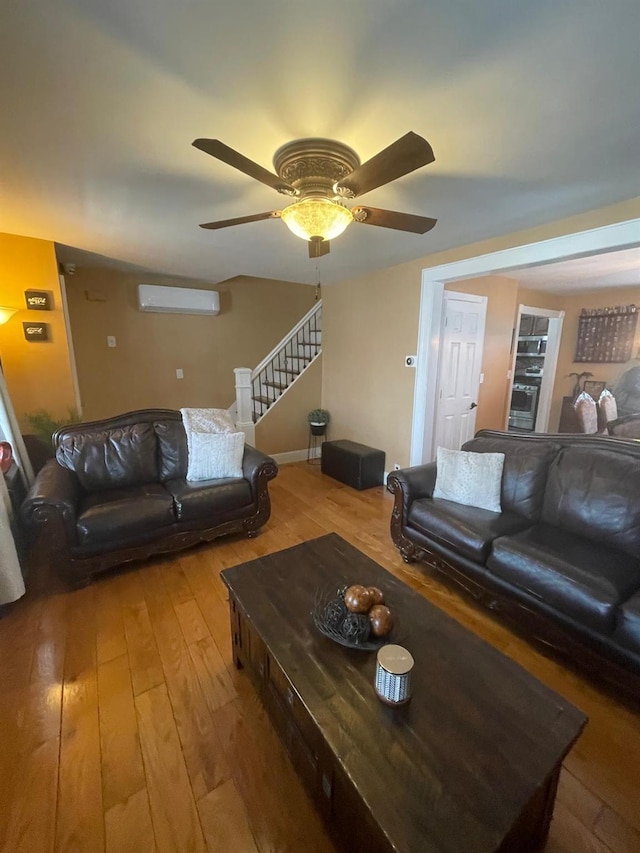 living room with wood-type flooring, a ceiling fan, stairs, and a wall unit AC
