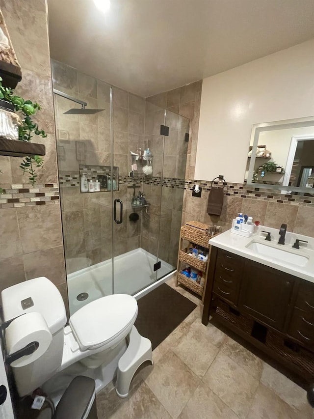 bathroom with toilet, tile walls, a shower stall, and vanity