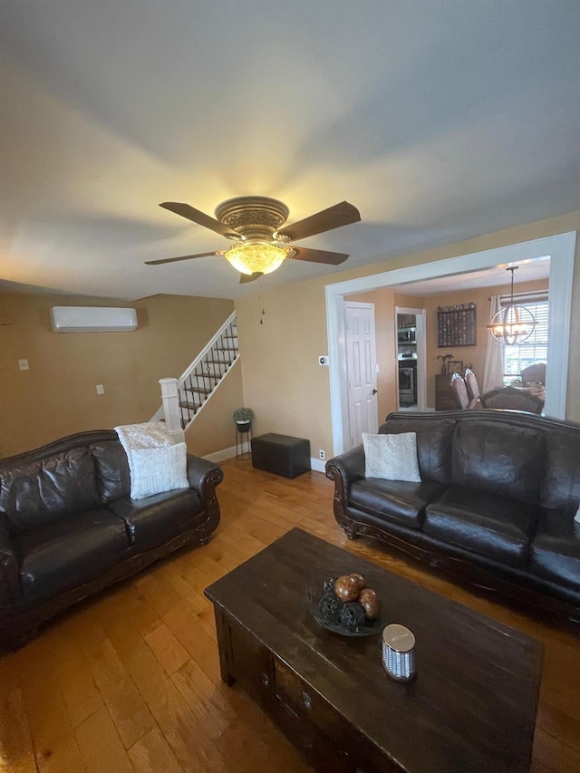 living area featuring baseboards, a wall mounted air conditioner, a ceiling fan, hardwood / wood-style flooring, and stairway