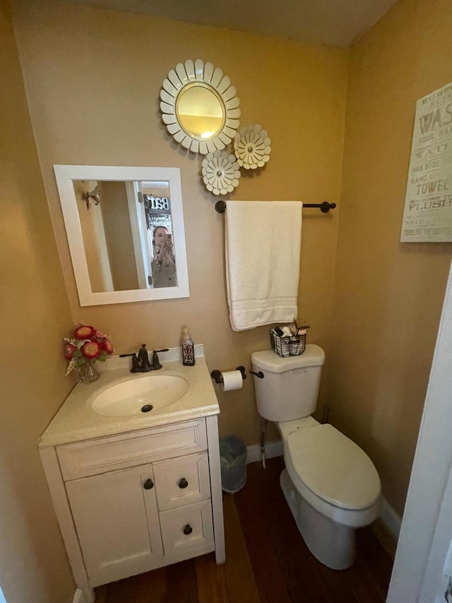 bathroom with toilet, vanity, wood finished floors, and baseboards