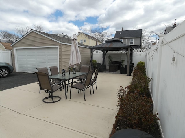 view of patio / terrace with a fenced backyard, a detached garage, an outdoor structure, a gazebo, and outdoor dining area