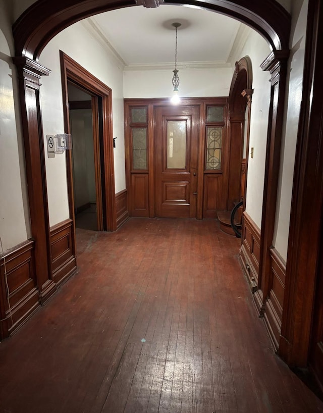 hallway with decorative columns, arched walkways, dark wood-type flooring, and a wainscoted wall