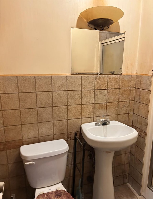 bathroom with toilet, a wainscoted wall, and tile walls