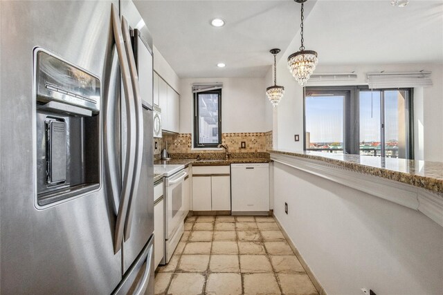 kitchen featuring white appliances, white cabinetry, a sink, stone tile floors, and a notable chandelier