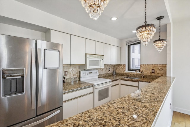 kitchen with a sink, decorative backsplash, a notable chandelier, white cabinetry, and white appliances