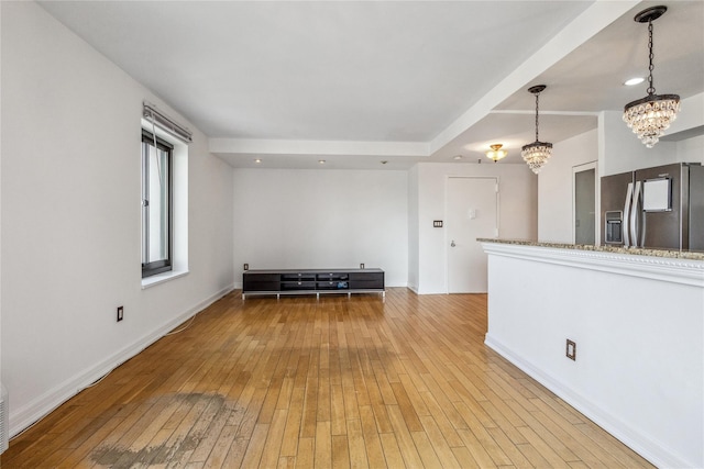 empty room with an inviting chandelier, baseboards, and light wood-style floors