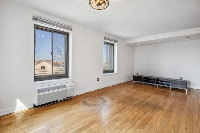 unfurnished room with wood finished floors, a wall mounted air conditioner, and baseboards