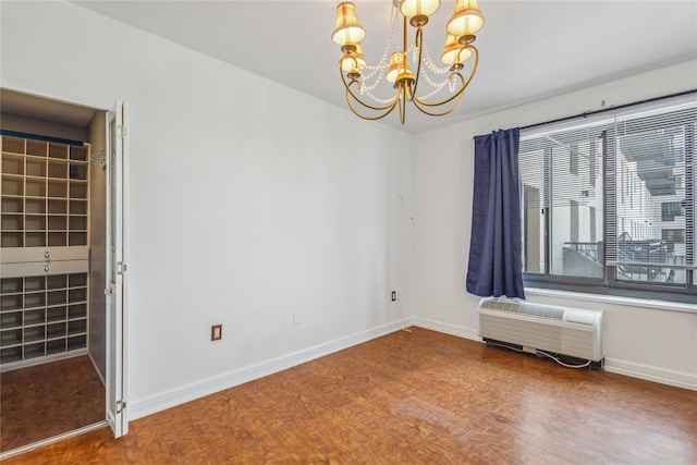 spare room with an AC wall unit, wood finished floors, a chandelier, and baseboards
