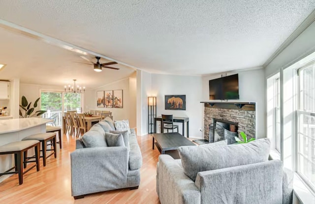 living room featuring a chandelier, a fireplace, light wood-style floors, and a textured ceiling