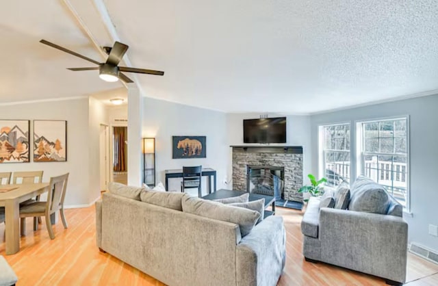 living area with baseboards, a stone fireplace, a ceiling fan, and visible vents