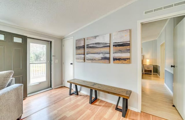 interior space featuring light wood finished floors, visible vents, a textured ceiling, and vaulted ceiling