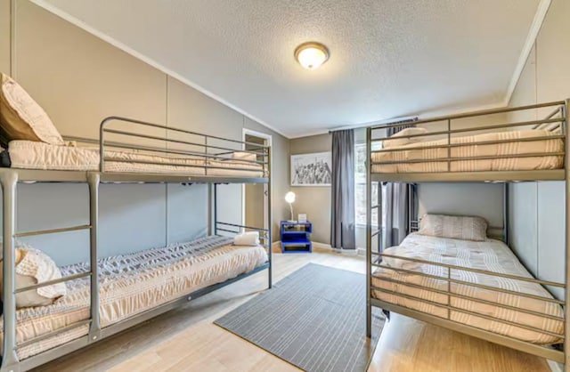 bedroom featuring baseboards, ornamental molding, a textured ceiling, lofted ceiling, and wood finished floors