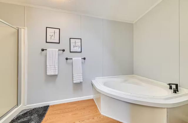 bathroom featuring a bath, ornamental molding, a stall shower, and wood finished floors