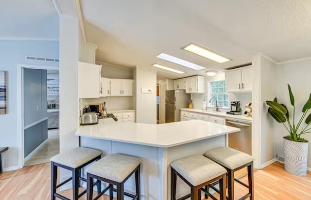 kitchen featuring light wood finished floors, a peninsula, a kitchen bar, and appliances with stainless steel finishes