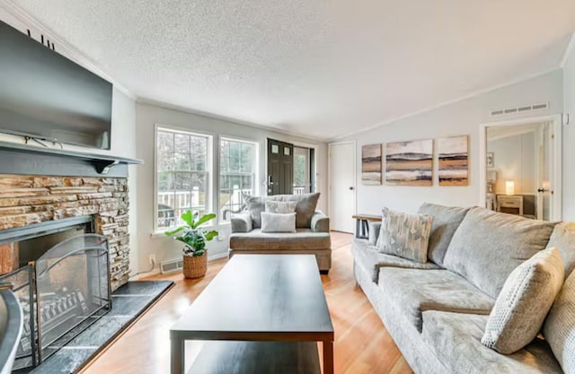 living room featuring visible vents, a stone fireplace, vaulted ceiling, and wood finished floors