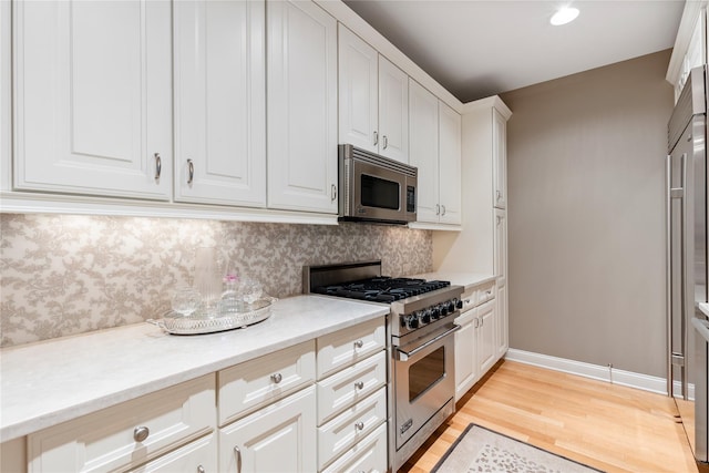 1 Christie Pl Unit 205W, Scarsdale, NY 10583 - kitchen with decorative backsplash, light wood-type flooring, baseboards, white cabinets, and appliances with stainless steel finishes