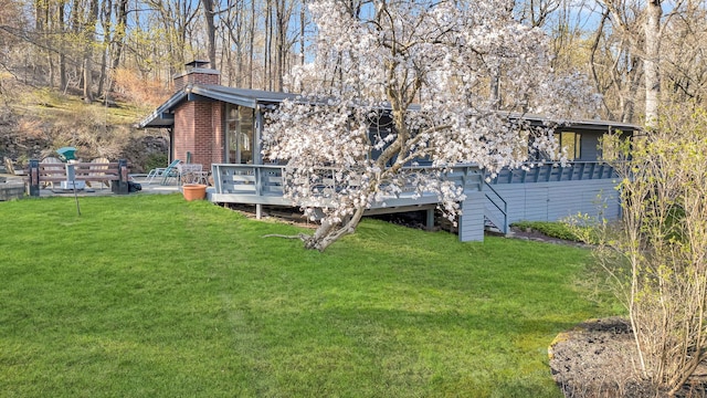 rear view of property with a chimney, a deck, and a lawn