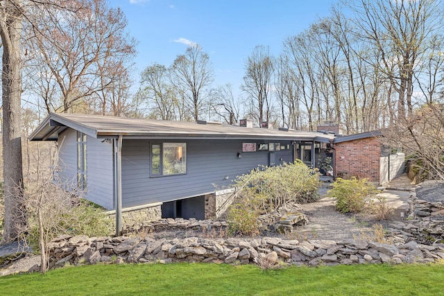 rear view of house featuring a chimney and a yard