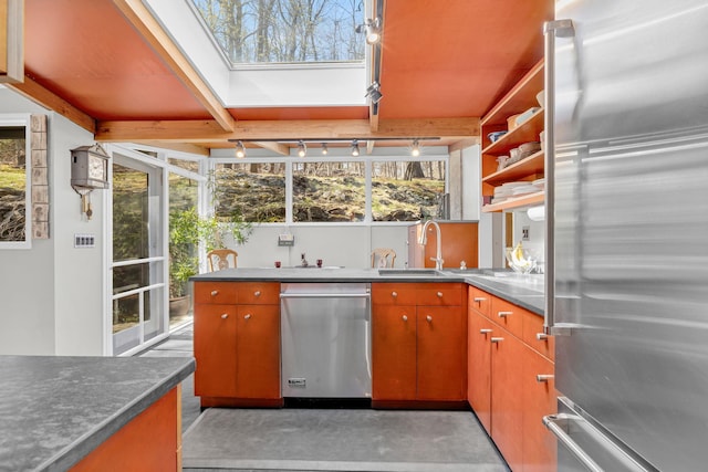 kitchen featuring open shelves, a sink, stainless steel appliances, track lighting, and a skylight