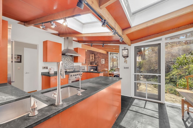 kitchen with beamed ceiling, stainless steel appliances, tasteful backsplash, track lighting, and wall chimney range hood