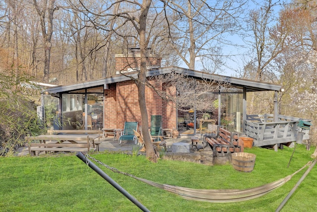 rear view of property with a chimney, brick siding, a lawn, and a patio area
