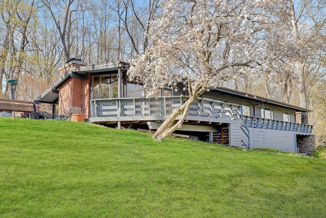 back of house featuring a chimney, a yard, a wooden deck, and a sunroom