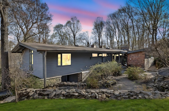 back of property featuring a yard, stone siding, and a chimney