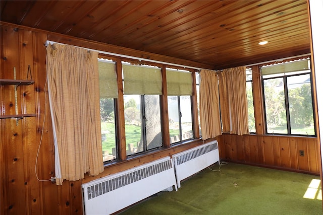 unfurnished sunroom with wooden ceiling, carpet floors, radiator heating unit, and wood walls