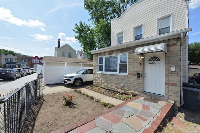 view of front of house with a detached garage, an outbuilding, fence, and stone siding
