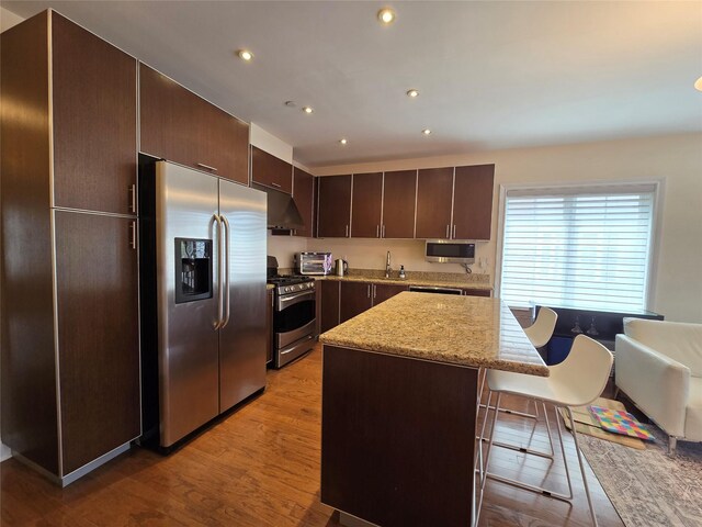 337 Park Cres, College Point, NY 11356 - kitchen with stainless steel appliances, dark brown cabinets, a breakfast bar area, light wood-type flooring, and a kitchen island