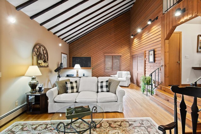 living area with high vaulted ceiling, wooden walls, wood finished floors, a baseboard heating unit, and stairs