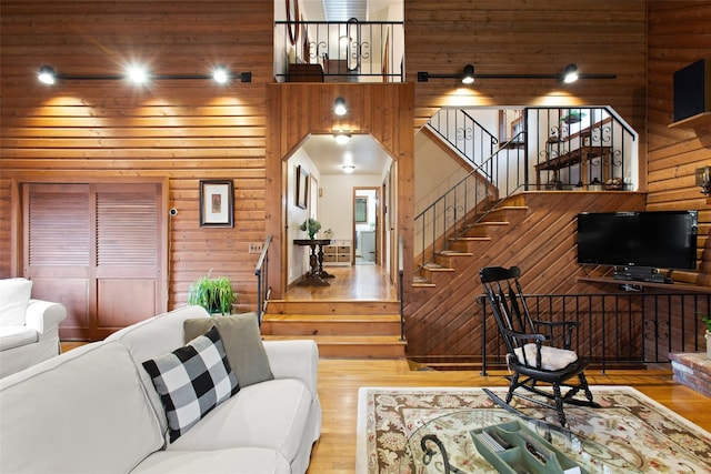 living area featuring a high ceiling, stairs, wood finished floors, and wooden walls