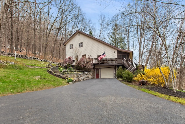 exterior space with a garage, stairway, a deck, a yard, and aphalt driveway
