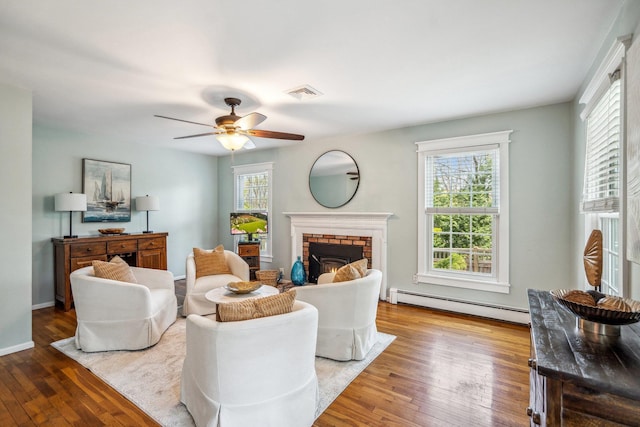 living area featuring a baseboard heating unit, visible vents, wood finished floors, ceiling fan, and a fireplace