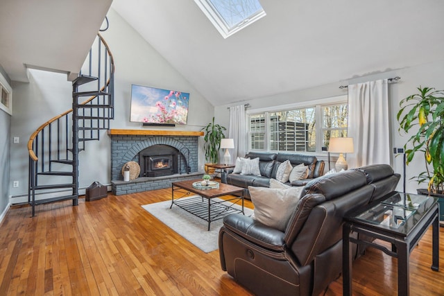 living room with high vaulted ceiling, a skylight, wood finished floors, stairs, and a fireplace