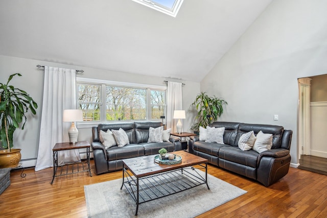 living room featuring a baseboard heating unit, wood finished floors, a skylight, and high vaulted ceiling