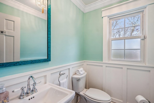 bathroom with a wainscoted wall, a sink, toilet, crown molding, and a decorative wall