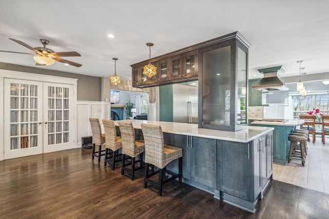 kitchen with ceiling fan, island exhaust hood, wood finished floors, appliances with stainless steel finishes, and a breakfast bar area