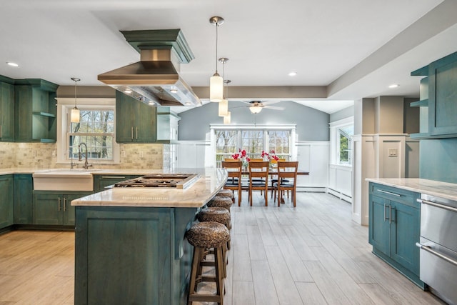 kitchen featuring island exhaust hood, green cabinetry, open shelves, a sink, and appliances with stainless steel finishes