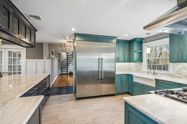 kitchen featuring decorative backsplash, light stone countertops, built in fridge, and a sink