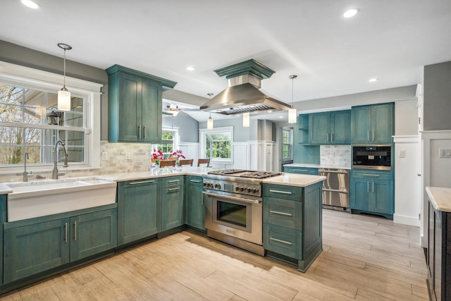 kitchen featuring a sink, wainscoting, island range hood, green cabinets, and appliances with stainless steel finishes