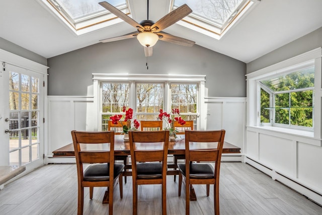 dining room featuring wainscoting, a baseboard radiator, a decorative wall, and a ceiling fan