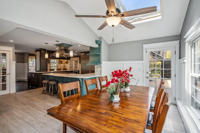 dining space featuring a wainscoted wall, wood finished floors, a ceiling fan, a baseboard heating unit, and a decorative wall