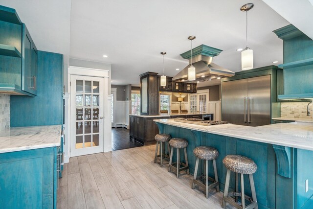 kitchen with a kitchen breakfast bar, stainless steel built in refrigerator, backsplash, light wood-style floors, and island range hood