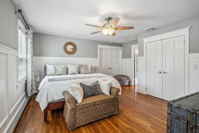 bedroom featuring a baseboard heating unit, wood finished floors, visible vents, and wainscoting