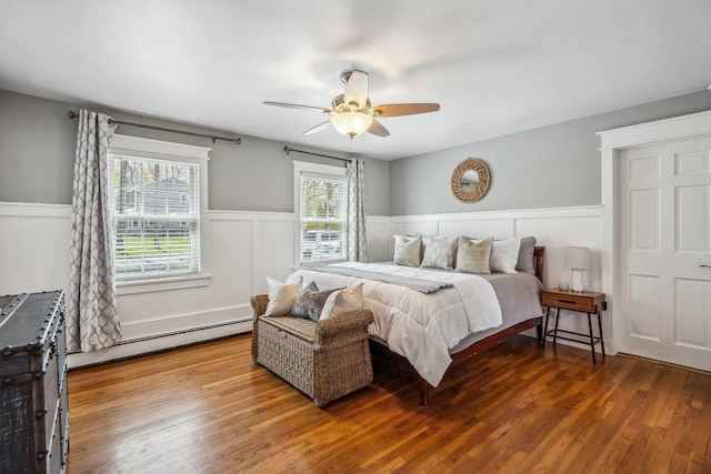 bedroom with a baseboard heating unit, wood finished floors, a wainscoted wall, and ceiling fan